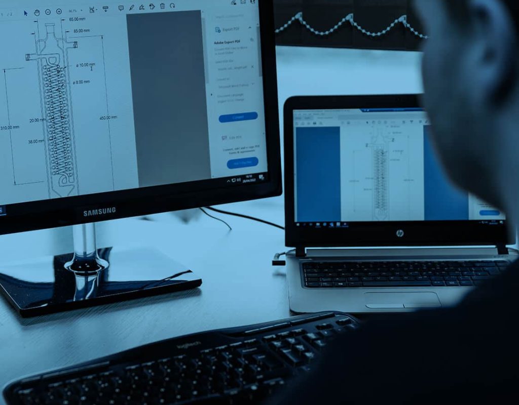 A professional working on multiple computer screens with data and analytics related to a glass reactors systems